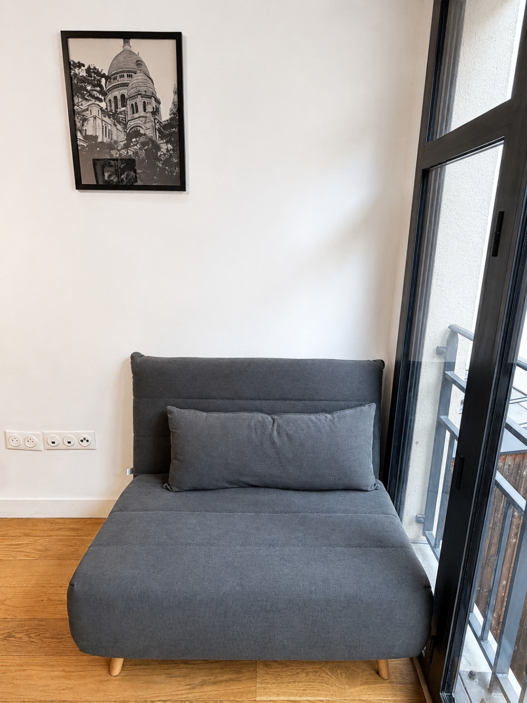 Espace salon avec canapé et bureau, baie vitrée donnant sur les toits parisiens